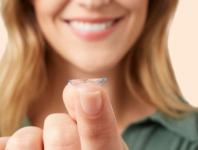 Plan rapproché sur une femme regardant une lentille posée sur son doigt avec un sourire aux lèvres. On ne voit pas ses yeux