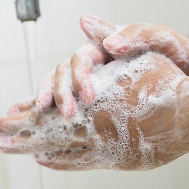 Gros plan sur des mains pleines de savon sous le robinet.