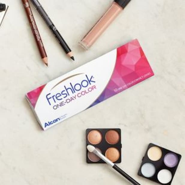 Une boîte de lentilles de couleur Freshlook One-Day Colour à côté de palettes de fard à paupières, crayons pour les yeux